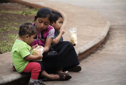 Three kids sit on a curb in Mexico while eating a snack. Margie Nea for Bread for the World.