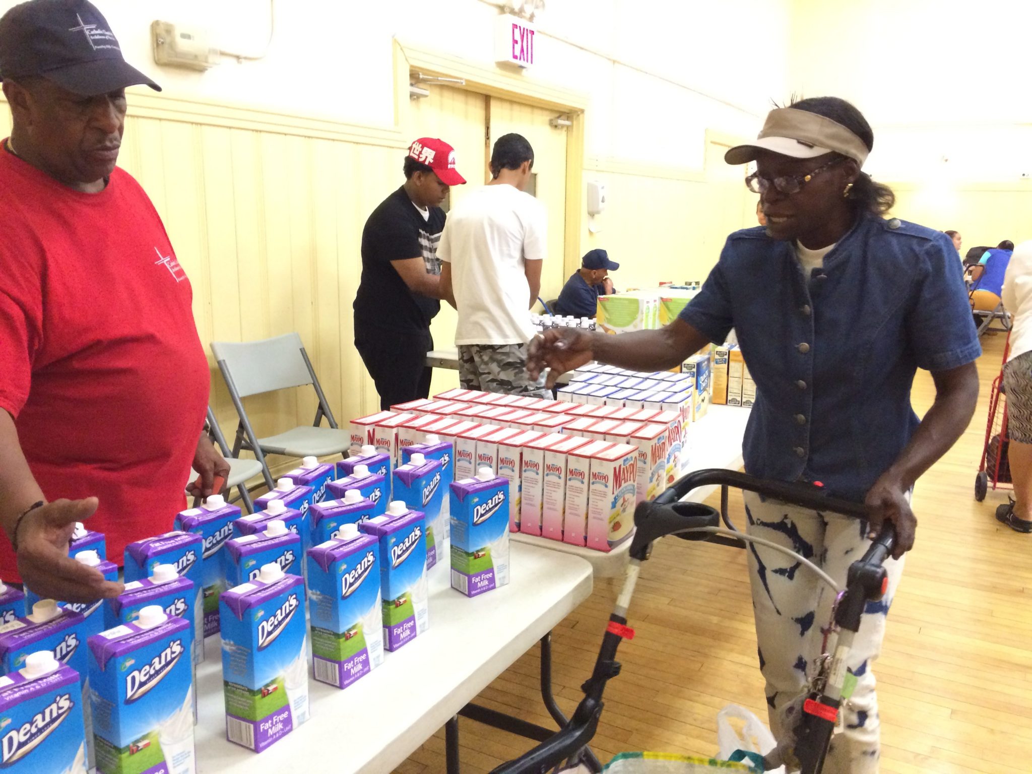 Susan La-Rose selects milk for her daughters at the food pantry at Catholic Charities' Lt. Joseph P. Kennedy Jr. Community Center in Harlem as volunteer Aubrey Woods looks on.