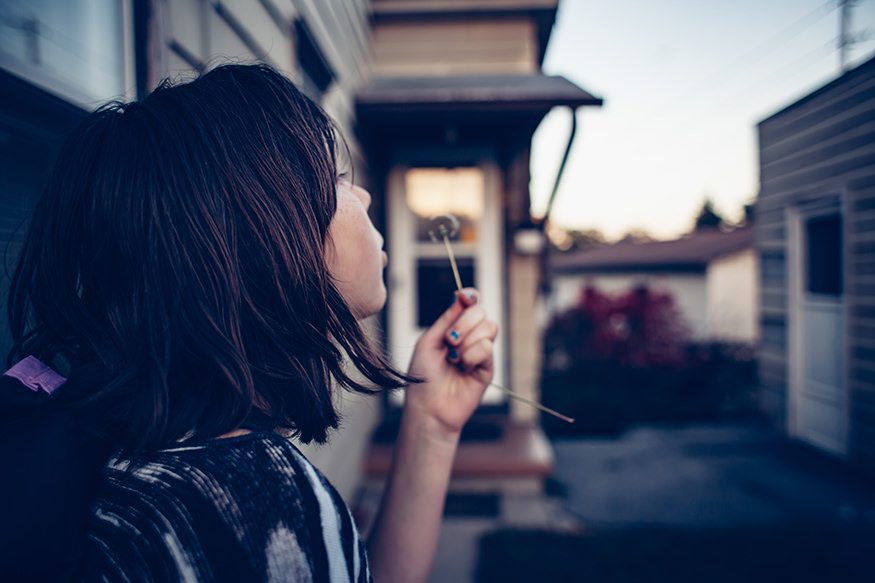 Arwen blows at a dandelion and makes a wish in front of the house. Joseph Terranova for Bread for the World.
